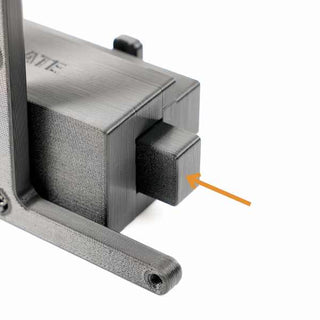 Close-up of a 3D-printed, black component with an arrow pointing to a rectangular section, attached to a vertical piece with visible layering.