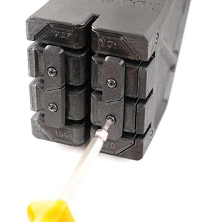 A screwdriver with a yellow handle is tightening a screw on a black mechanical device with visible cog-like parts.