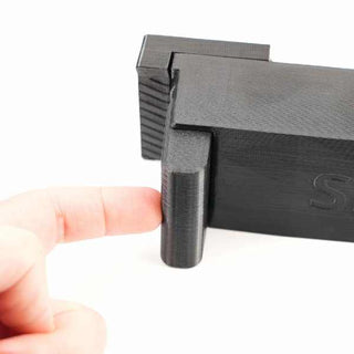A finger touches the latch of a 3D-printed black hinge.
