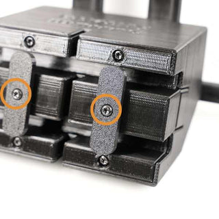Close-up of a black mechanical assembly with multiple interlocking segments and visible screws. Two orange circles highlight specific screws in the structure.