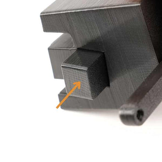 Close-up of a textured black 3D-printed object with a protruding rectangular section. An orange arrow points to the front face of the protruding part.