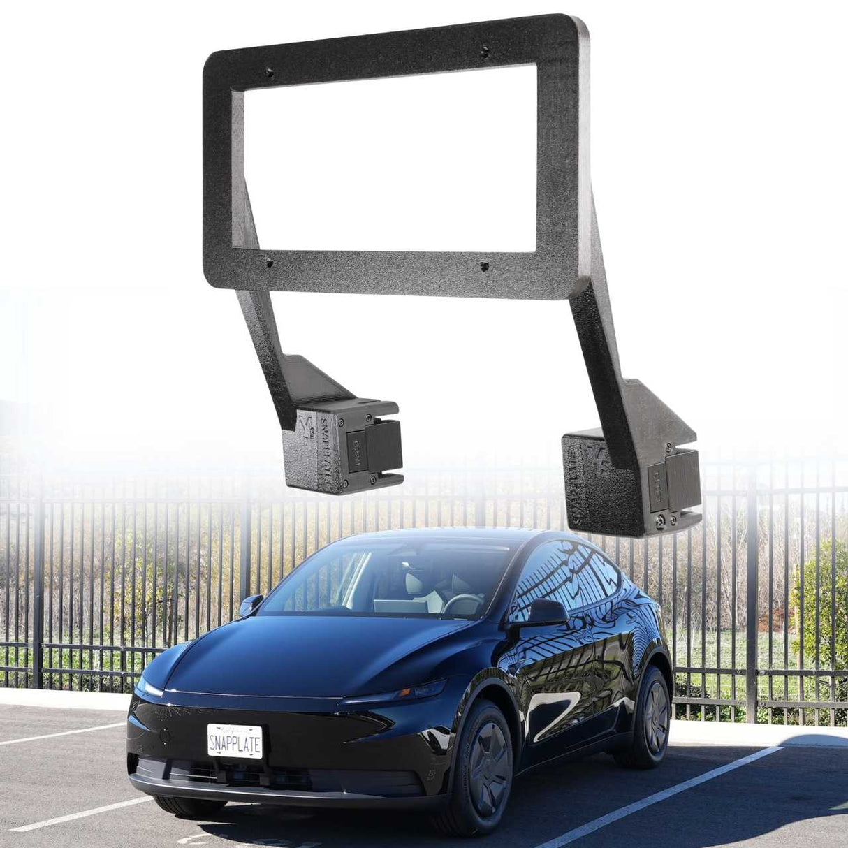 An EveryAmp Tesla Model Y SnapPlate Front License Plate Holder is displayed above a parked black car by a metal fence on a sunny day.