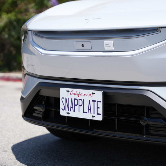 Close-up of a white car’s front with a California plate reading “SNAPPLATE,” featuring EveryAmp’s Polestar 3 SnapPlate No-Drill Front License Plate Holder, made from recycled PETG and designed for an emblem-free grille.