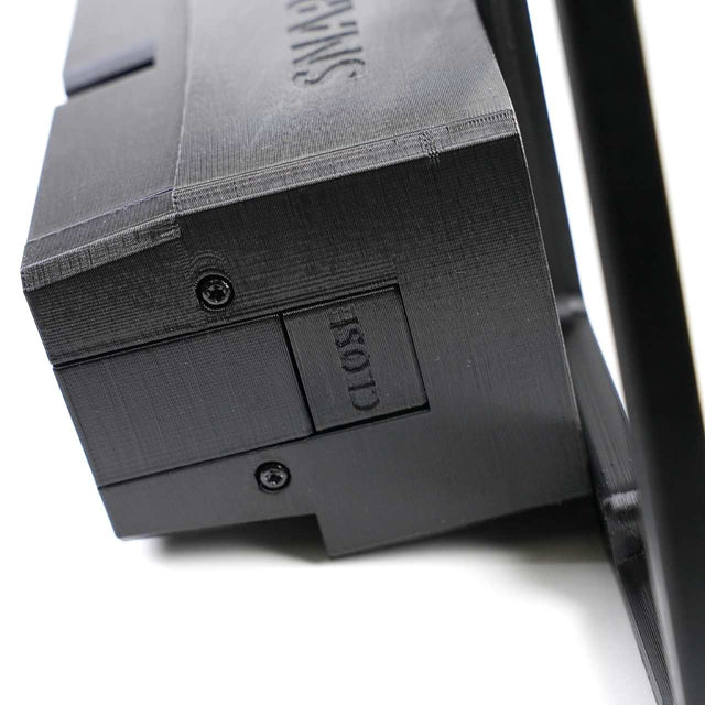 Close-up of a black plastic device with a sliding switch labeled CLOSE and visible screws on its surface.