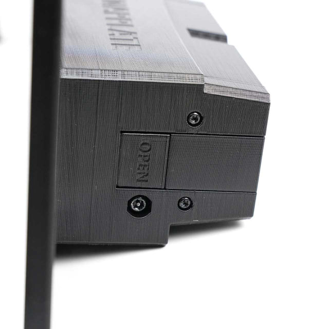 Close-up of a black plastic device with a textured surface, visible screws, and a small panel labeled OPEN next to a hexagonal socket.