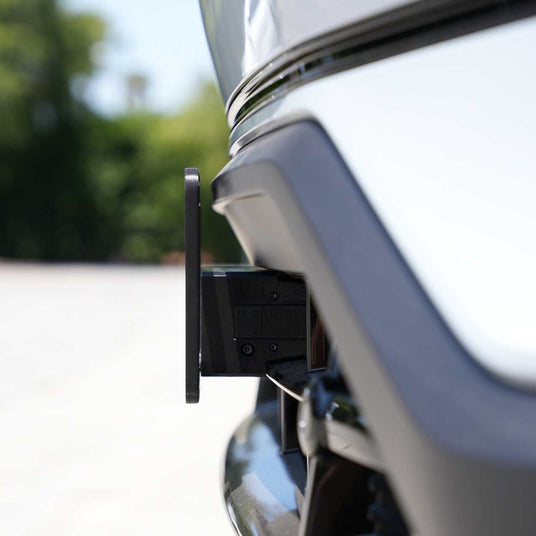 Close-up of a car’s front bumper with a license plate holder attachment, photographed outdoors in daylight.