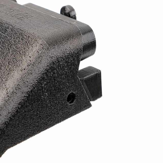 Close-up of a black 3D-printed object with a textured surface, featuring a protruding section and a small hole.