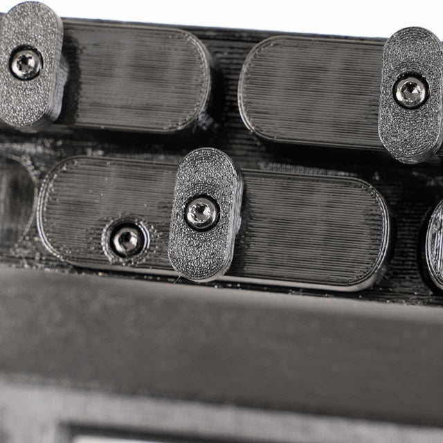 Close-up of a black mechanical component with multiple oval-shaped parts and screws, featuring a textured surface.