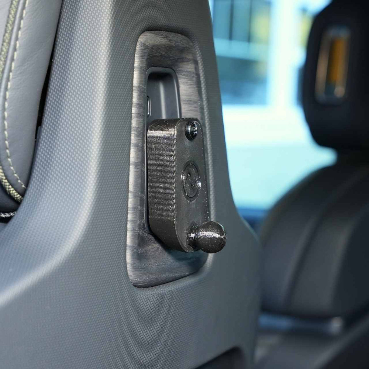 Close-up of a car seat headrest with an EveryAmp Back Seat Tablet/Phone Mount Anchor for Rivian R1T and R1S, featuring a small black 3D-printed ball mount device attached to the seat back.