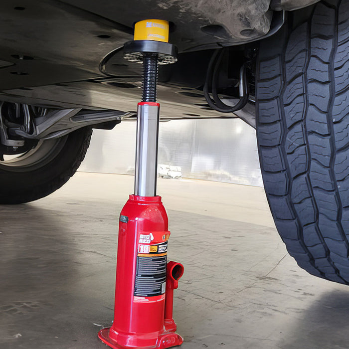 A red hydraulic bottle jack elevates a vehicle, with one large tire visible on the right, set on a concrete surface.