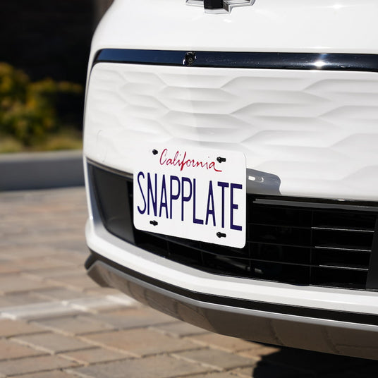 Close-up of a white car showing a California license plate with the text SNAPPLATE, mounted on the front bumper.