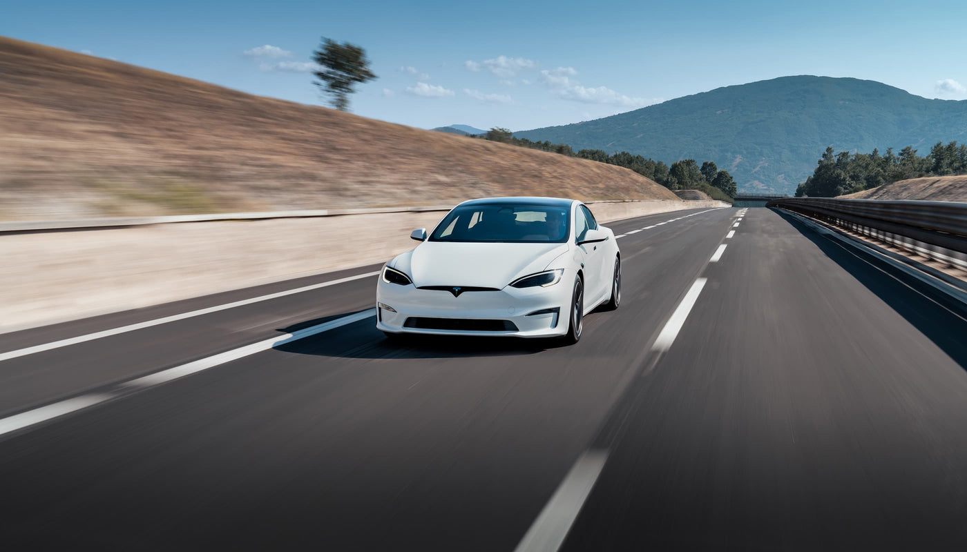 A white car driving on an empty highway with mountains and a blue sky in the background.
