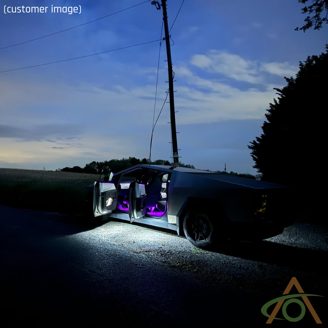 An illuminated futuristic car with open doors, featuring Abstract Oceans Ultrabright Lights for Cybertruck in purple, is parked on a rural road under a cloudy sky at night.