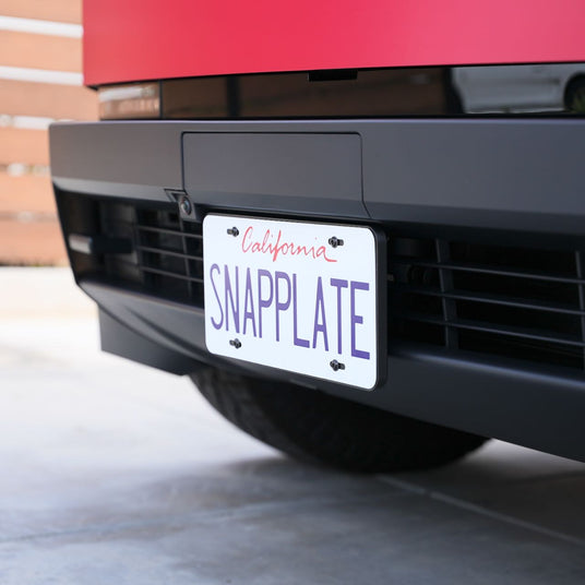 Close-up of a California license plate on a red vehicle with the text SNAPPLATE in bold purple letters, mounted on a sleek, modern bumper.