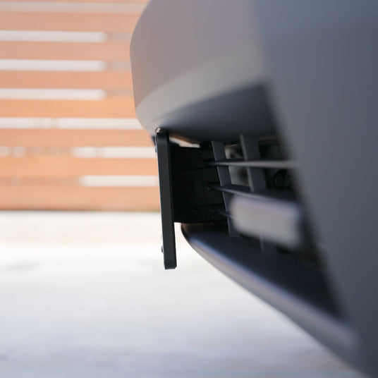 Close-up of a cars front bumper featuring an exposed panel or compartment opening on a blurred garage door background.