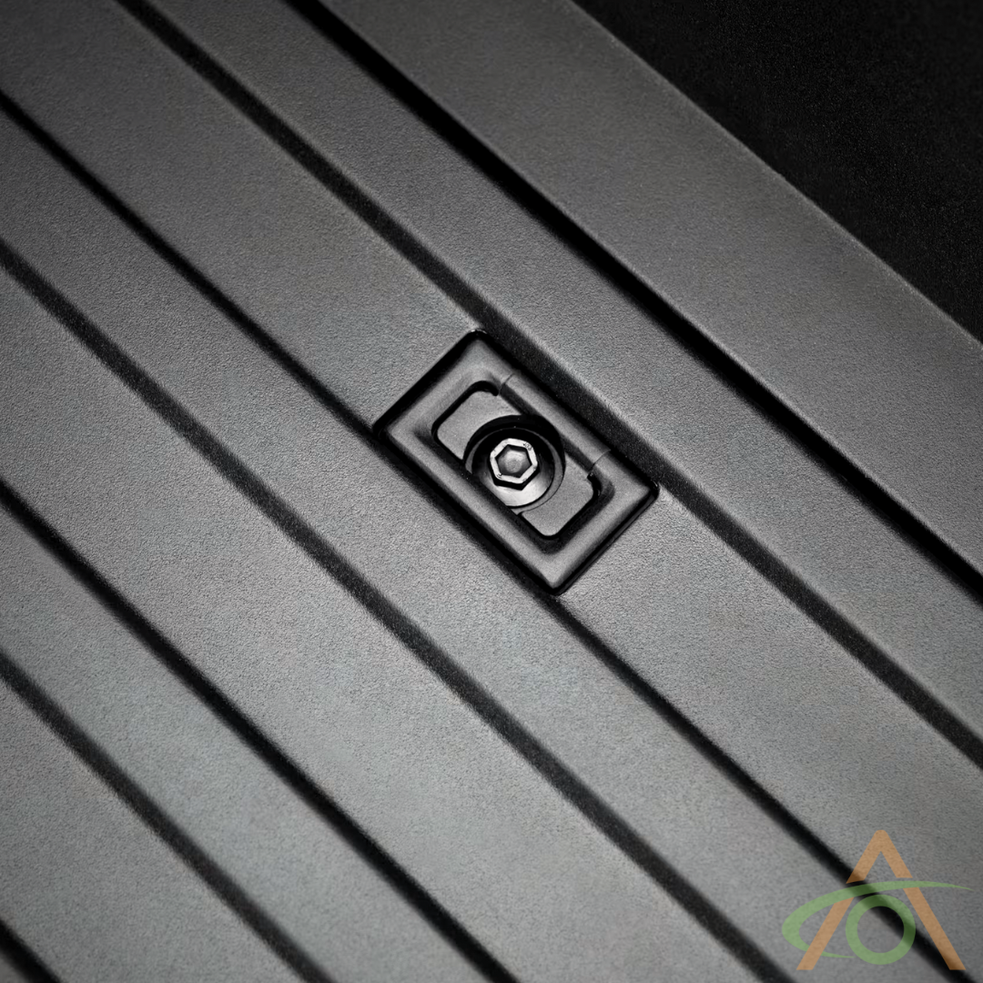 Close-up of a textured black, heavy-duty aluminum surface featuring ridged parallel lines and a rectangular recessed screw. A transparent logo with overlapping shapes in the bottom right corner mirrors the robust design of Abstract Oceans Cybertruck L-Track Accessories.