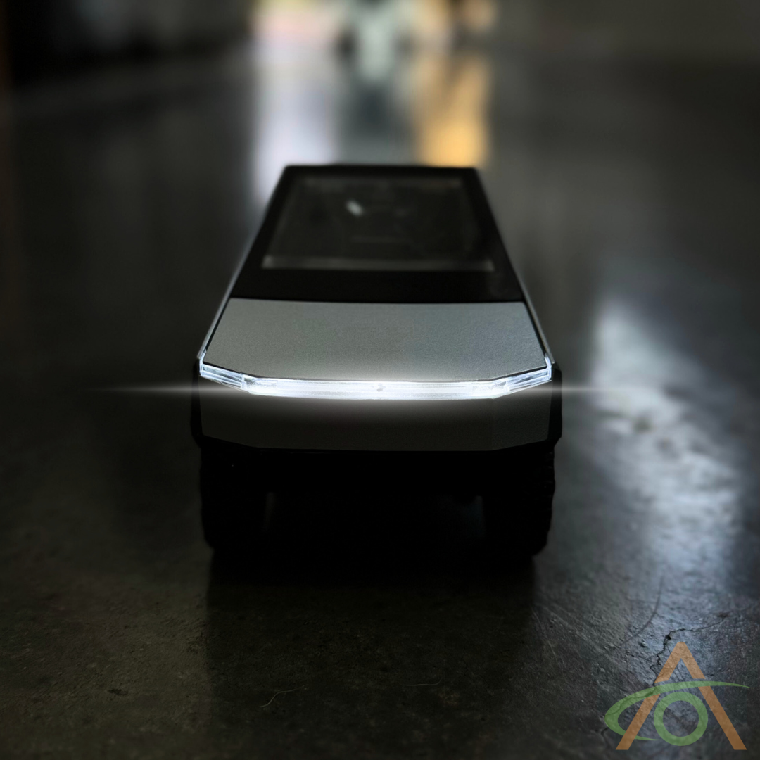 In a dimly lit space, the 1:24 Scale Cybertruck + Cyberquad Diecast by Abstract Ocean is photographed, highlighting its illuminated headlights and modern design.