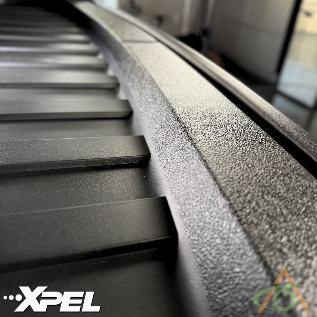Close-up of a textured, dark-toned surface featuring the Abstract Ocean logo in the bottom left, showcasing their Ultra-Tough Xpel Armor Frunk Protection for Cybertruck.