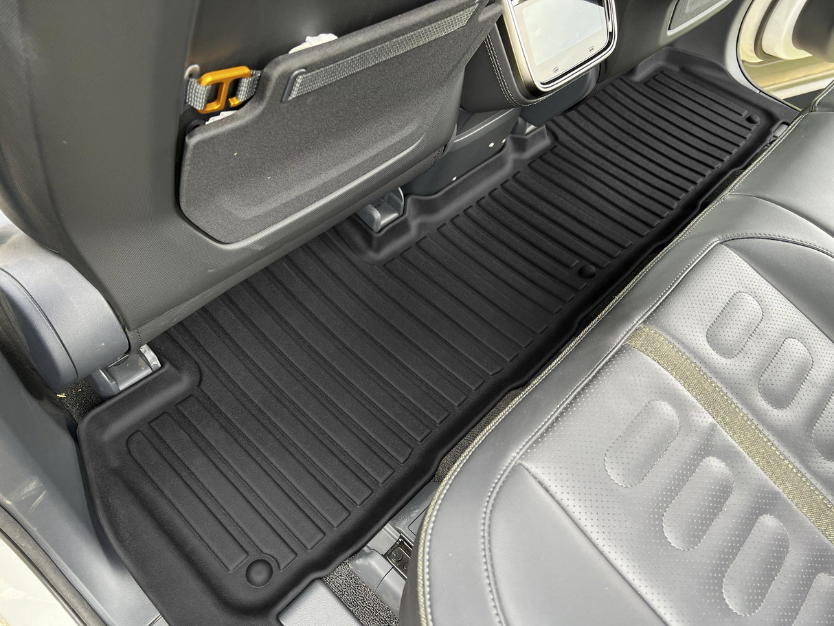 The LinerX Floor Mats for 2022-2024 Rivian R1S, crafted from durable Thermoplastic Elastomer, fully cover the rear floor of an R1S and extend seamlessly across the area, revealing parts of the seat backs and cushions.