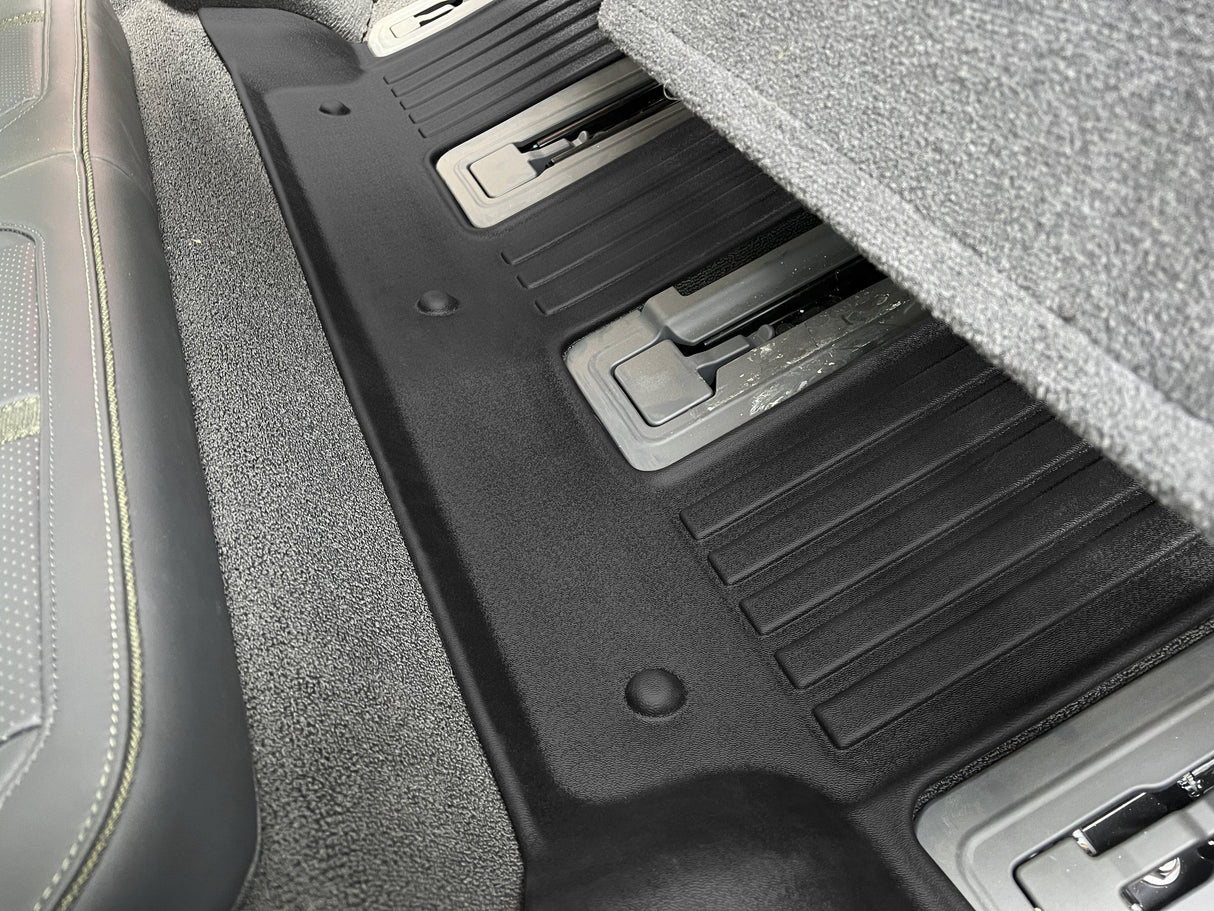 A close-up of a folded car seat in the Rivian R1S shows storage compartments beneath, resting on a LinerX Floor Mat for 2022-2024 models, ensuring durability and style.