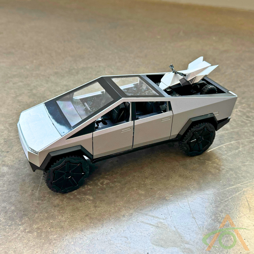 The 1:24 Scale Cybertruck + Cyberquad Diecast by Abstract Ocean, featuring a silver angular design, an open cargo bed, black wheels, and a pull-back action for dynamic display, rests on a beige surface capturing the essence of futuristic transport.