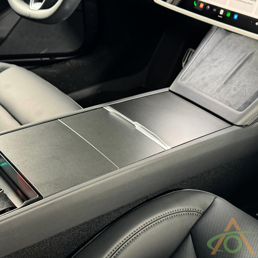 Close-up of a car's center console with black leather seats and part of a touchscreen, featuring the Abstract Ocean Center Console Vinyl Wrap for Refreshed Model 3 & Y, made with premium 3M 2080 film for style and protection.