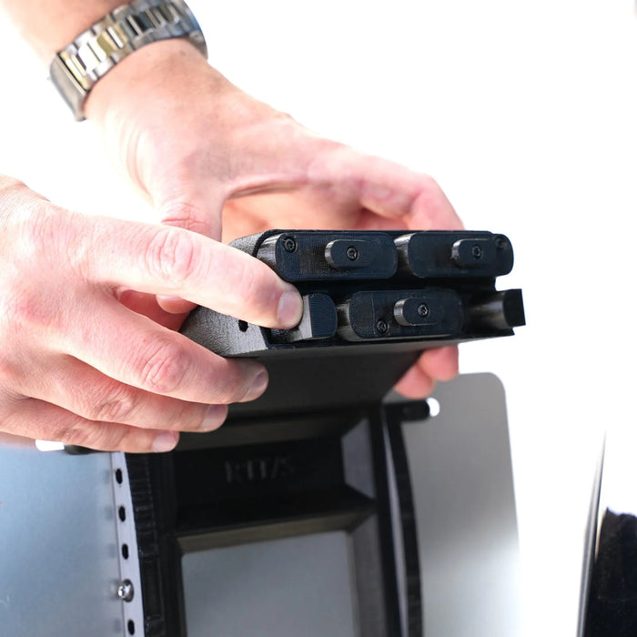 Hands adjusting a black mechanical device with multiple cylindrical components against a white background.