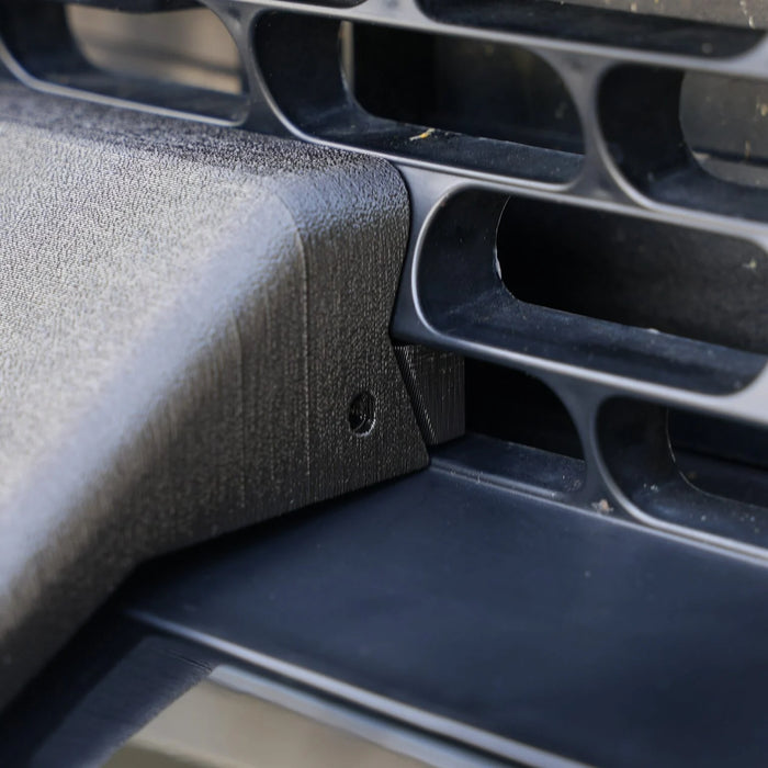 Close-up of a black object with rectangular vents and a slanted edge, featuring a small round screw on the corner.