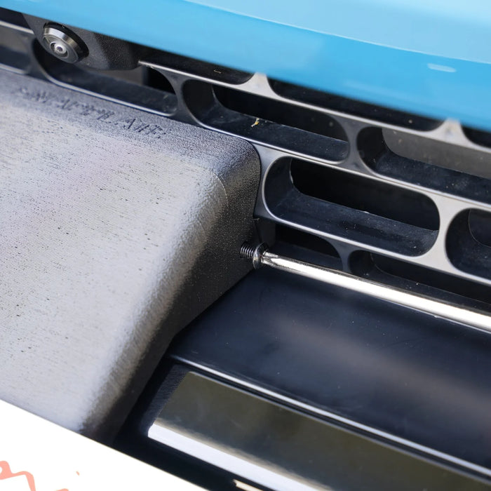 Close-up of a black metal screw partially unscrewed from a car grille next to a blue panel.