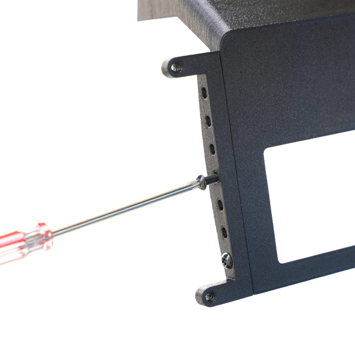 A screwdriver is tightening a side screw on a black metal bracket with a series of holes and a rectangular cutout.