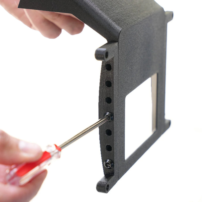 A person uses a red-handled screwdriver to assemble or adjust a black plastic frame with multiple holes and a rectangular cutout.