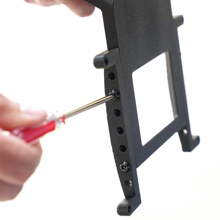 Person using a red-handled screwdriver to insert a screw into a black metal bracket with multiple holes.