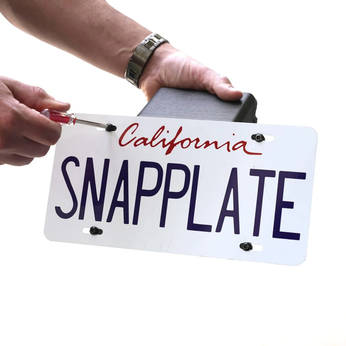Hands holding a California license plate with SNAPPLATE written on it, using a screwdriver to attach it to a black holder.