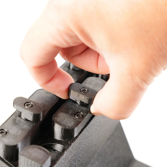 A hand adjusts a small screw on a black mechanical device with multiple slots.
