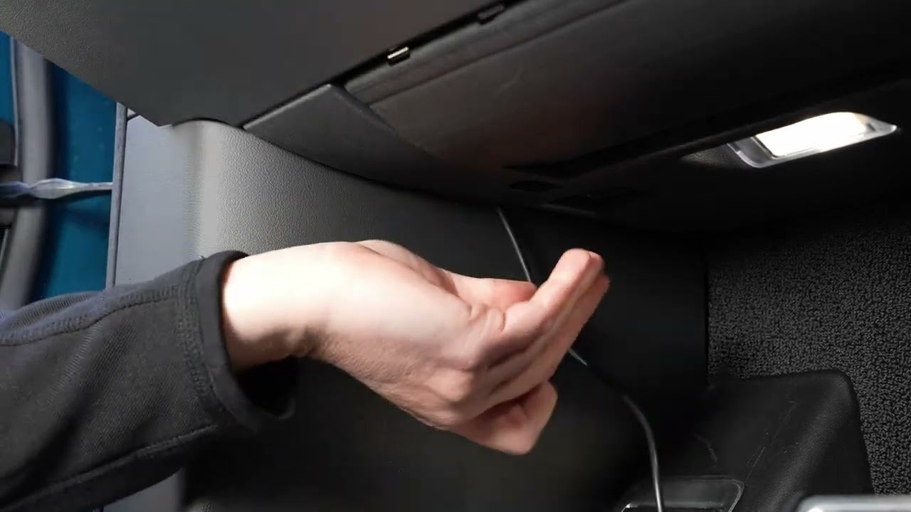 A persons hand opening a cars glove compartment with a cable nearby.