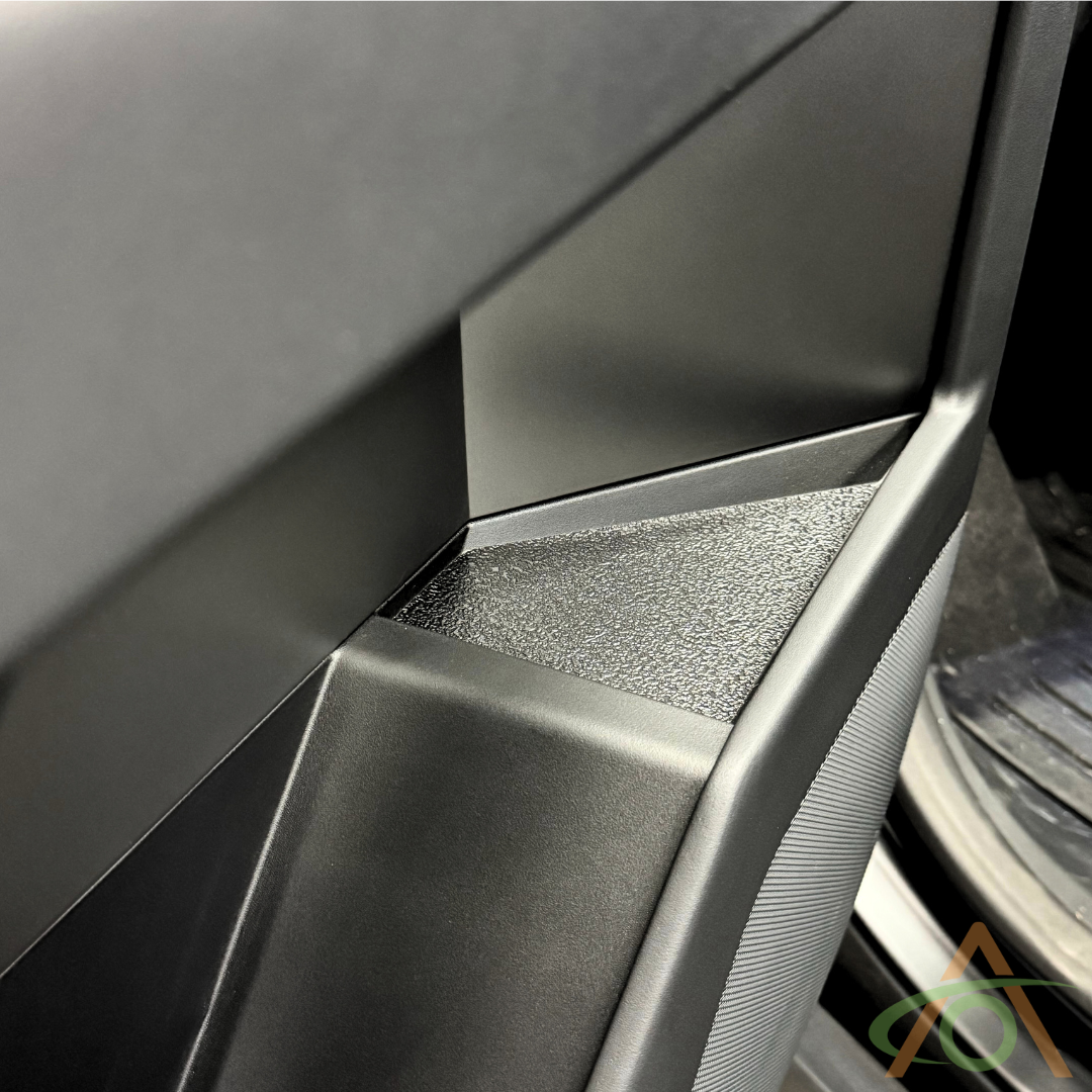 Close-up of a modern car door interior featuring sleek black surfaces and a textured storage compartment, offering robust protection similar to Abstract Oceans Xpel Armor Door Inserts for Cybertruck.