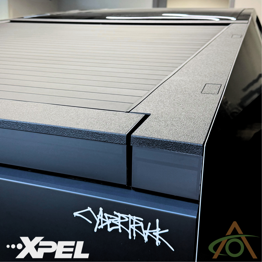 The Cybertruck tailgate features Ultra-Tough Xpel Armor Bed Protection by Abstract Ocean, with a textured cover that displays the XPEL logo and stylized Cybertruck text, offering seamless integration for enhanced weather protection.