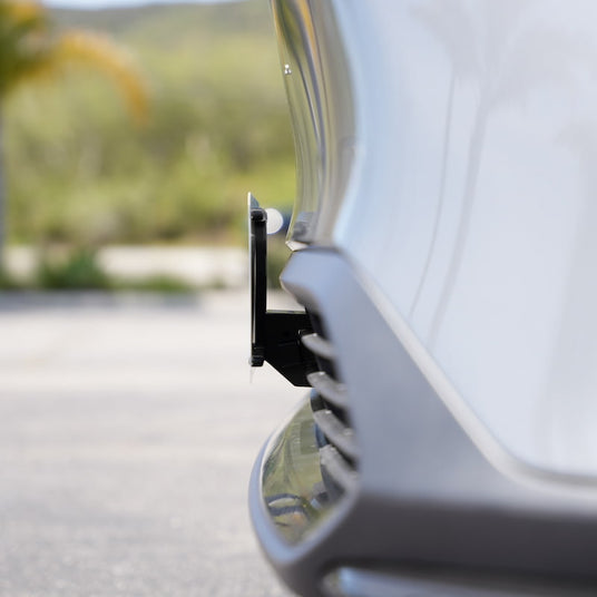 Close-up of a cars parking sensor on the front bumper, with a blurred natural background and a palm tree in the distance.