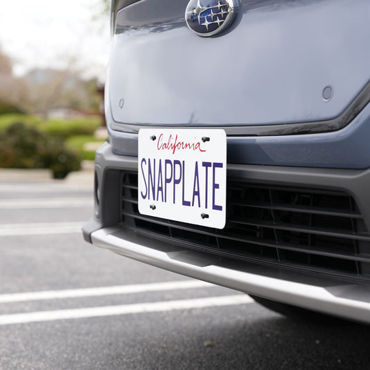 Close-up of a cars front license plate displaying the word SNAPPLATE with a California label, parked on an asphalt surface.