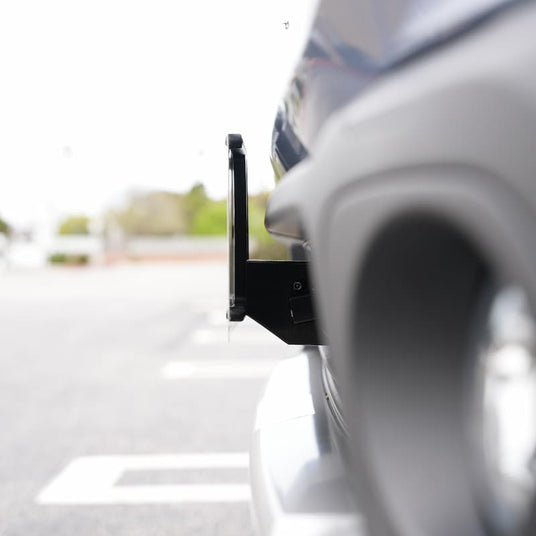 Close-up of a cars front bumper with a prominent tow hook attached, in a parking area with blurred background.