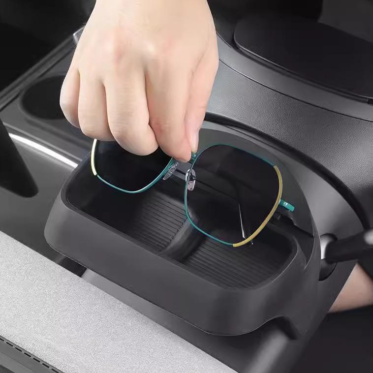 A hand places sunglasses into the Tesery Official Store Sunglasses & Phone Holder Organizer for Model Y Juniper, neatly showcasing its sleek in-car organization near the center console.