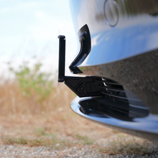 Close-up of a black front camera mounted on a cars bumper, facing the road, with a blurred natural background.