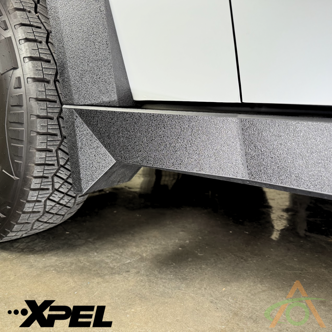 A close-up of a Cybertruck’s tire and textured body panel featuring Abstract Oceans Ultra-Tough Xpel Armor Rocker Protection. The Xpel Armor logo is visible at the bottom left for robust film, with another logo at the bottom right.