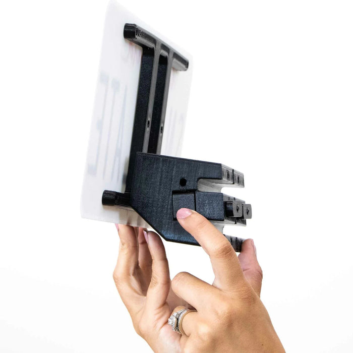 A hand demonstrating the installation of a black wall mount bracket attached to a white sign, against a plain white background.