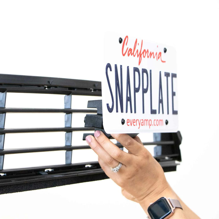 Hands attaching a SnapPlate license plate holder to a vehicle grille, showing a California license plate.