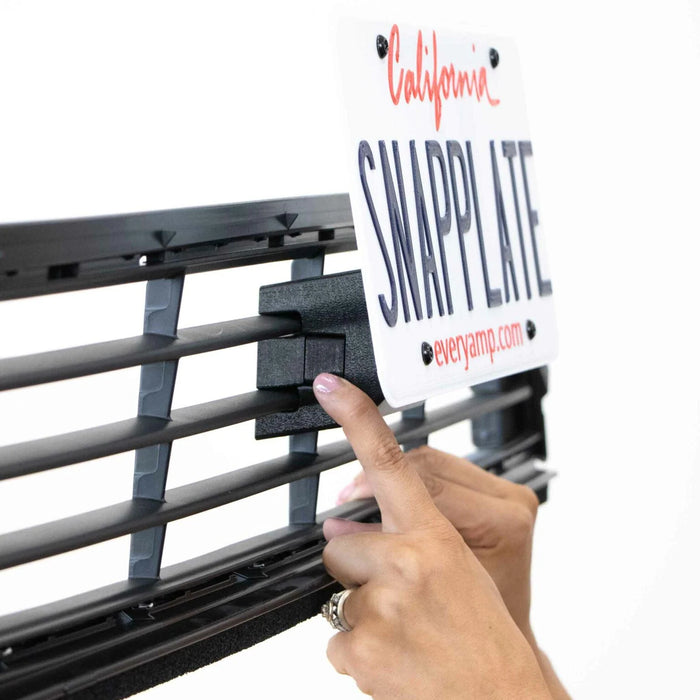 Person attaching a removable license plate holder labeled SNAPPLATE onto a car grille.