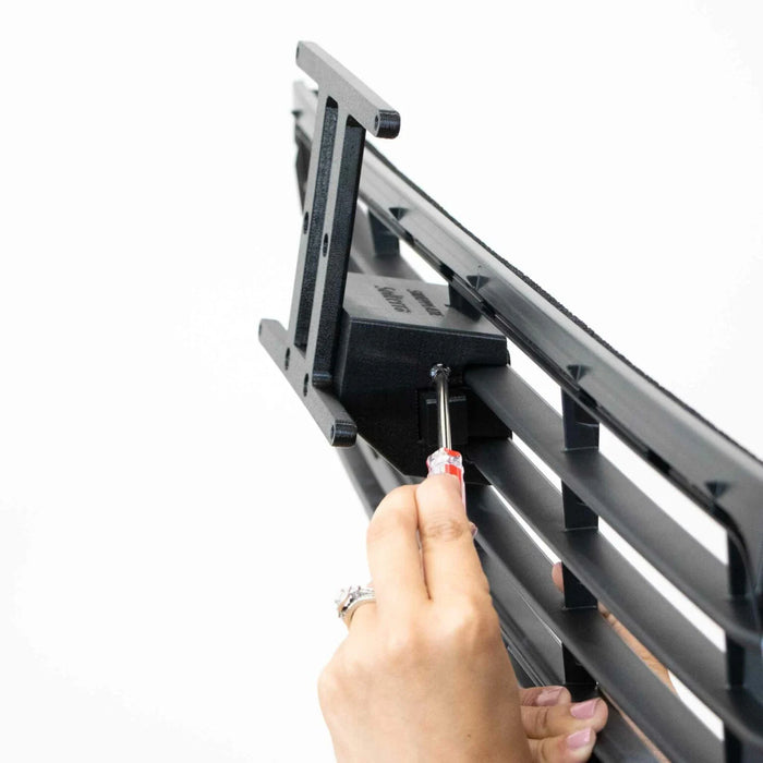 A person uses a screwdriver to attach a black phone holder onto a horizontal vent mount.
