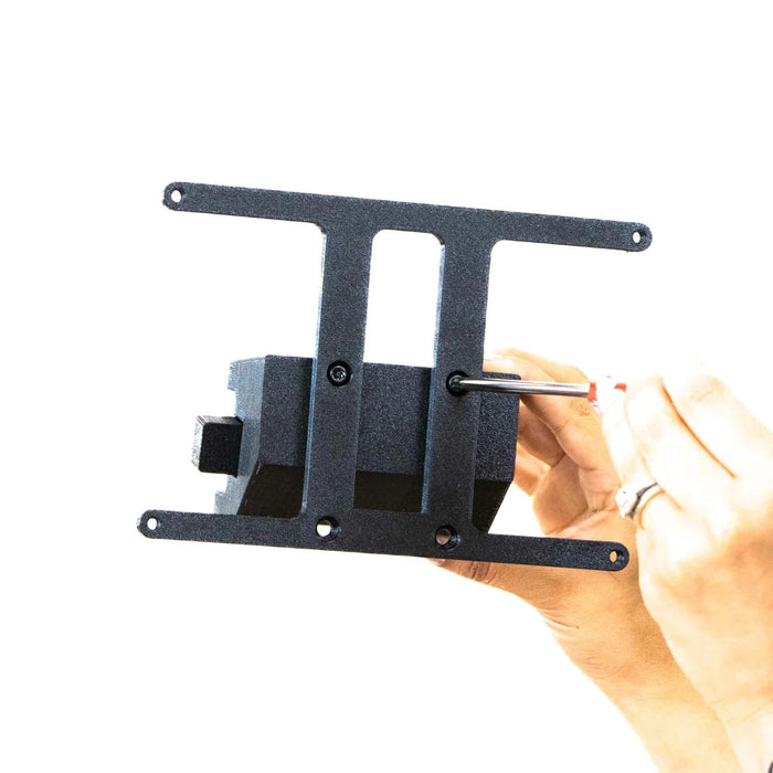 Hands assembling a black metal bracket using a wrench, against a white background.