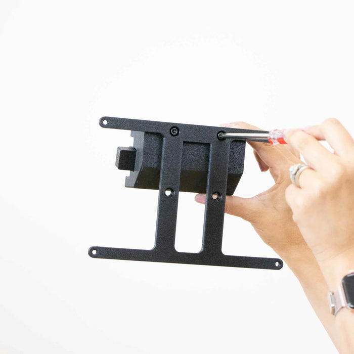 Hands using a screwdriver to assemble a black metal bracket against a plain white background.