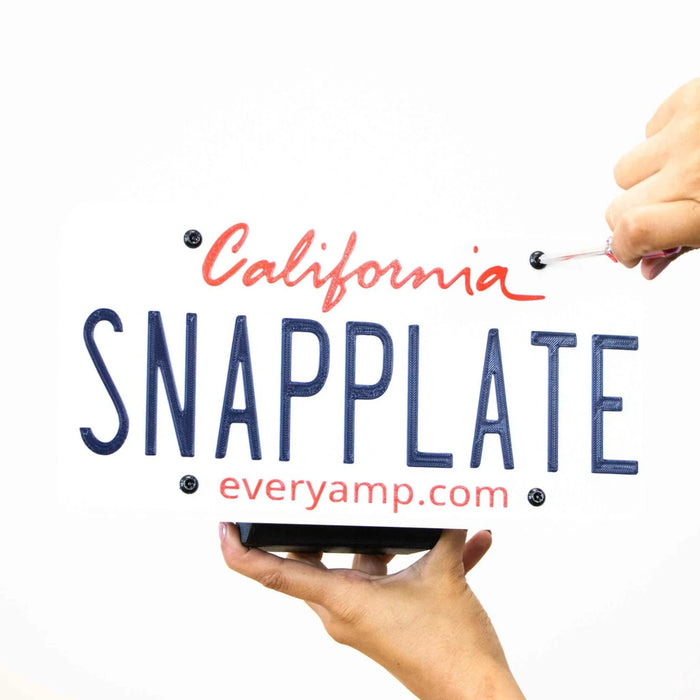 Hands hold a novelty California license plate reading SNAPPLATE, with everyamp.com below.
